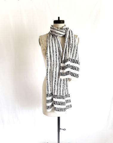 Vertical stripes on long part of black and white scarf with 3 horizontal stripes on the hem.